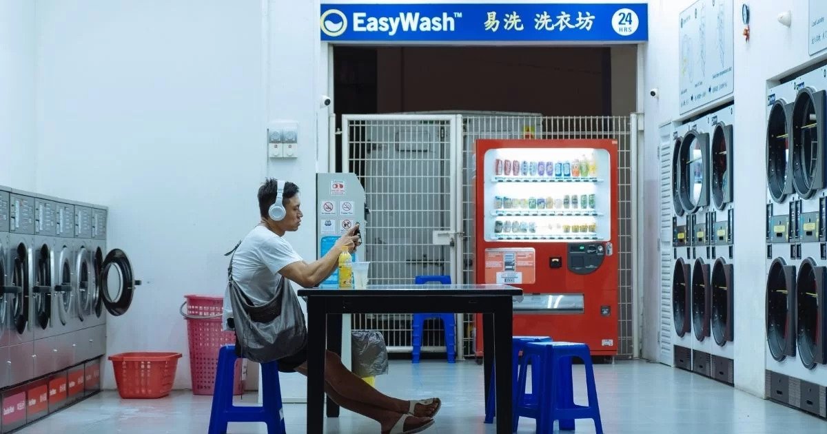 a guy playing his phone in the coin laundry shop
